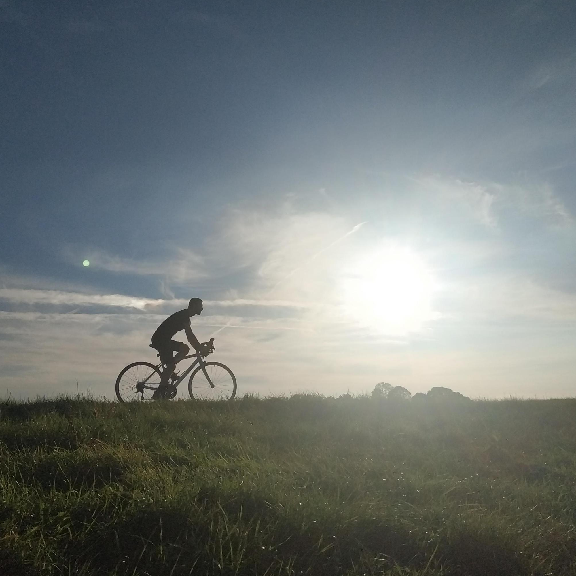 Me as a silhouette cycling my typically Dutch bike atop a typically Dutch dike, while the sun sets in the background